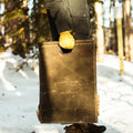 A person holding a waxed canvas firewood carrier. 