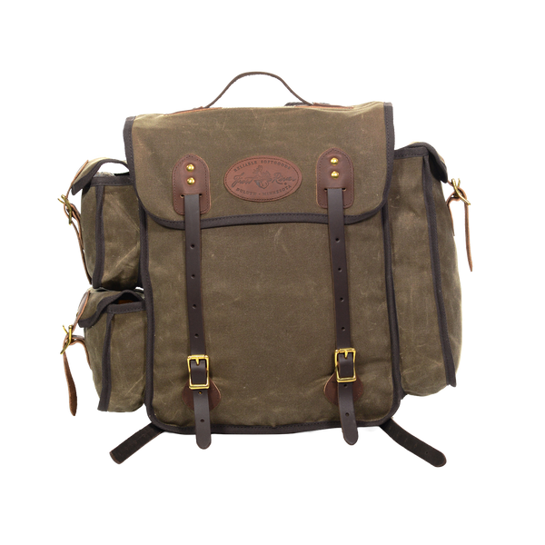 A waxed canvas backpack with dark brown leather straps and trim, featuring a central flap pocket with brass-tone buckles and a circular leather logo patch.