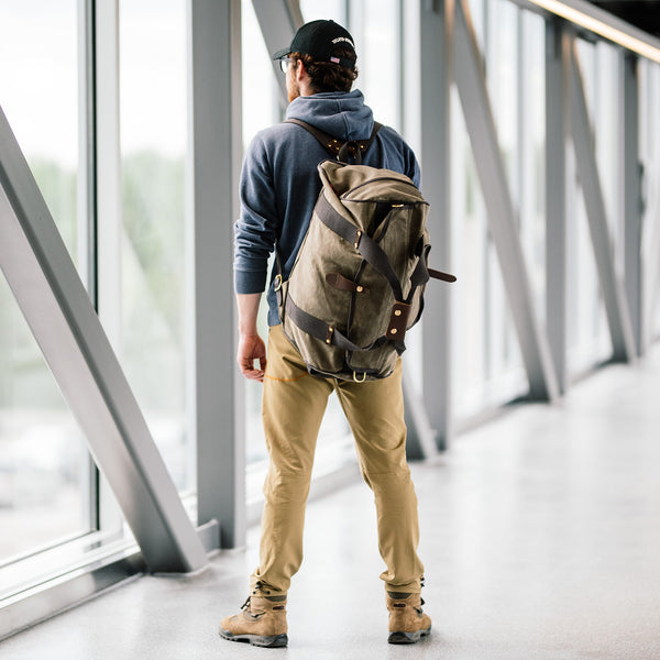 A man wearing the Explorer Duffel ESB which is a waxed canvas duffle bag equipped with back straps. 